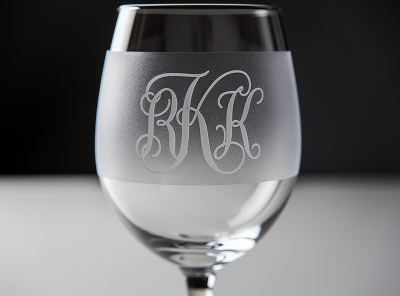 Wine glass with elegant white frosted laser engraved design on the side held against a dark background to highlight the frost contrast