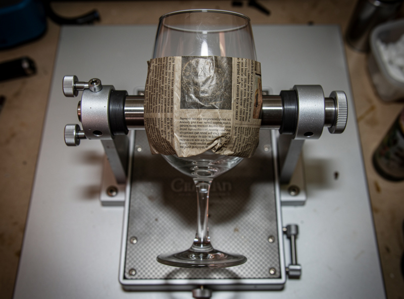 Wine glass with damp newspaper covering the engraving area being prepared for laser engraving on a rotary attachment