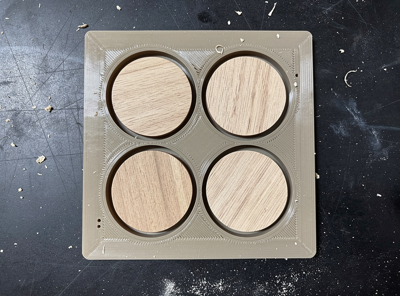 3D-printed wooden coaster jig with six circular cutouts holding wood blanks for batch engraving