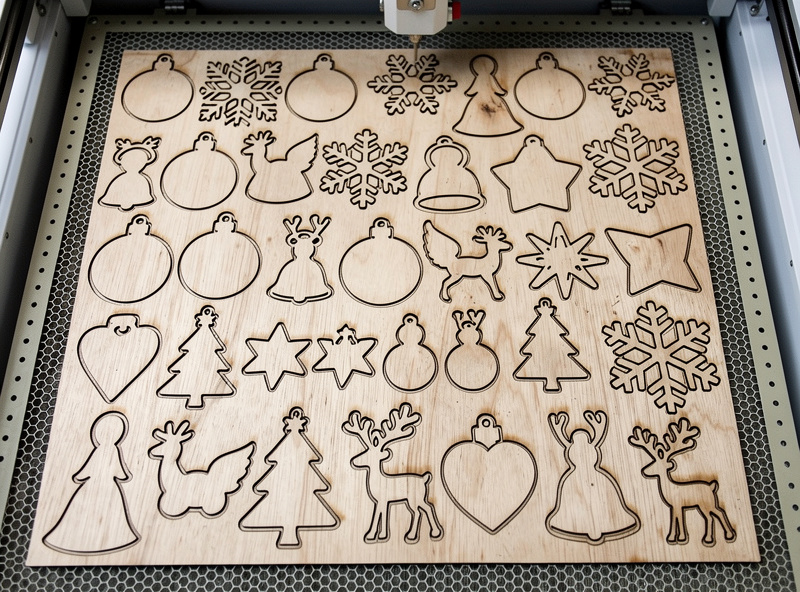 A sheet of 3mm birch plywood nested with many laser-cut Christmas ornament shapes on a laser bed