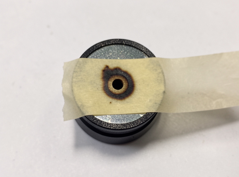 Masking tape over a CO2 laser mirror mount showing a pulse burn mark used for alignment