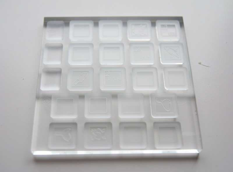 A laser-engraved acrylic test tile showing a row of stepped engraving depths from light frost to deep channel under raking light
