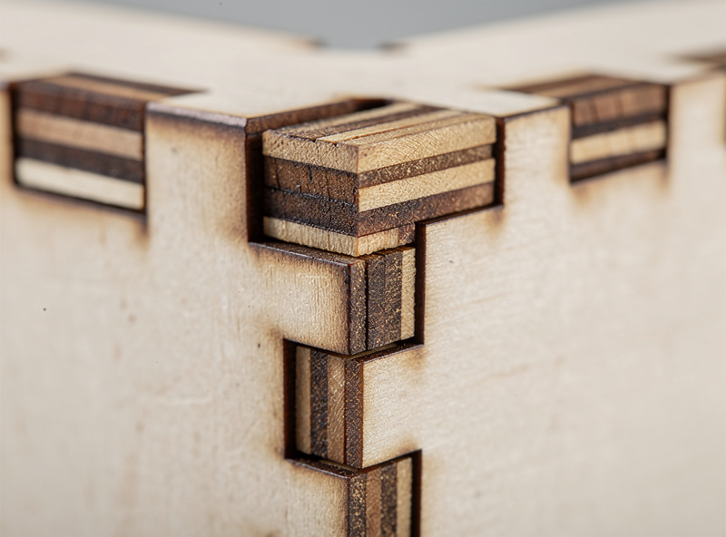 A finished laser-cut plywood finger-joint box with a lid, showing tight interlocking finger joints