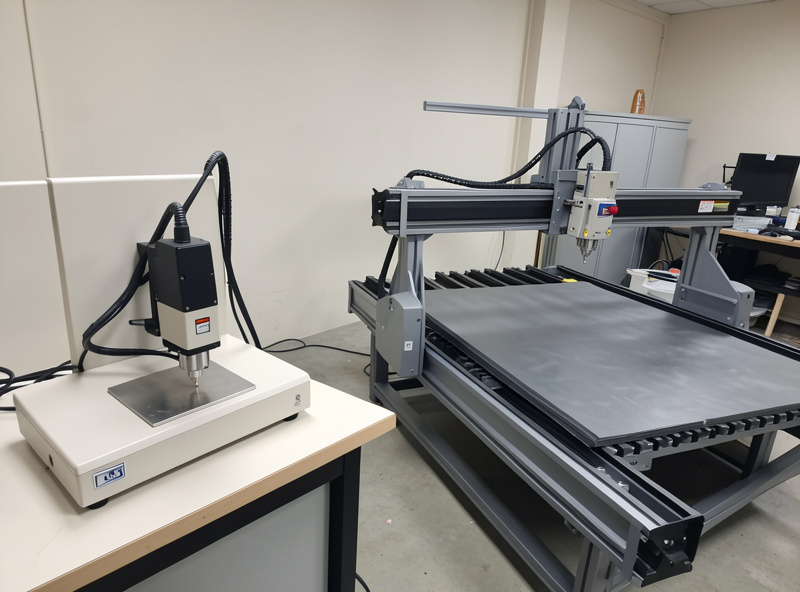 A compact galvo fiber marker beside a large gantry laser on rails in a workshop