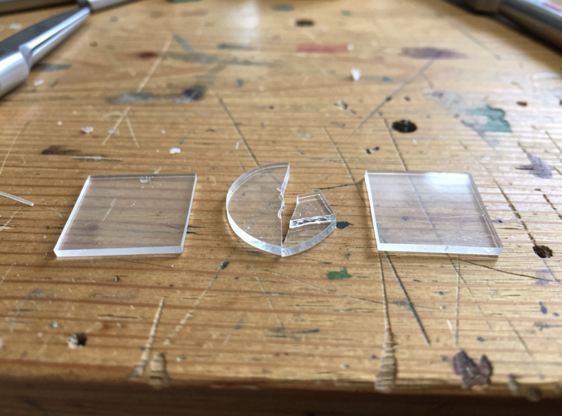 Three clear plastic offcuts arranged on a workbench representing cast acrylic, extruded acrylic, and polycarbonate, illustrating how similar look-alikes can be