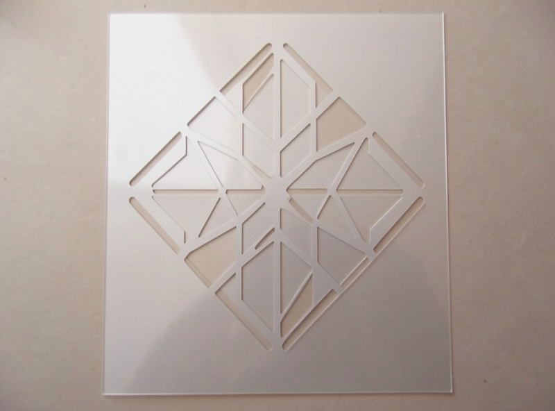 A finished laser-cut mylar airbrush stencil held up to the light showing crisp clean cut detail