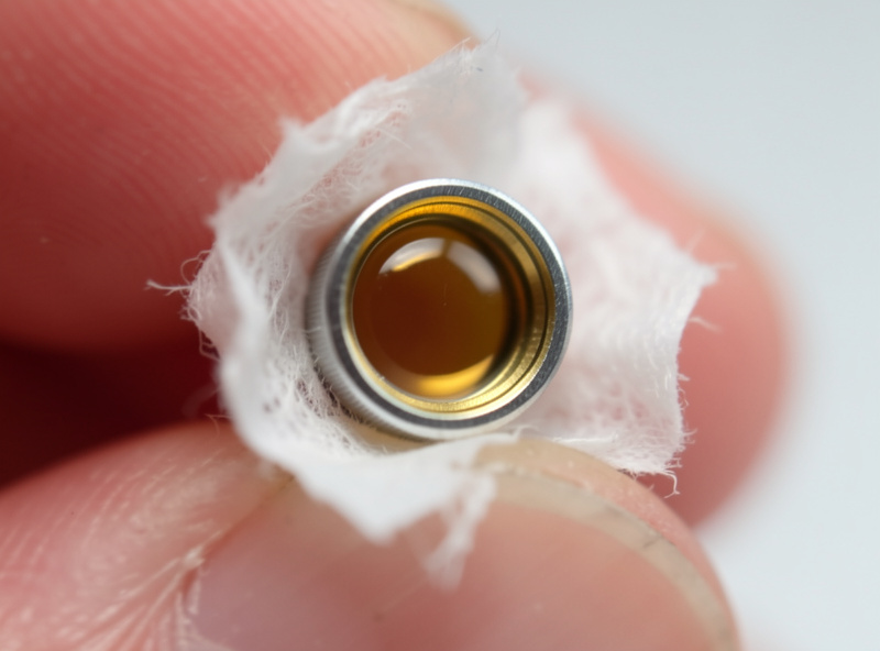 A laser focusing lens removed from its holder being cleaned with lens tissue and solvent