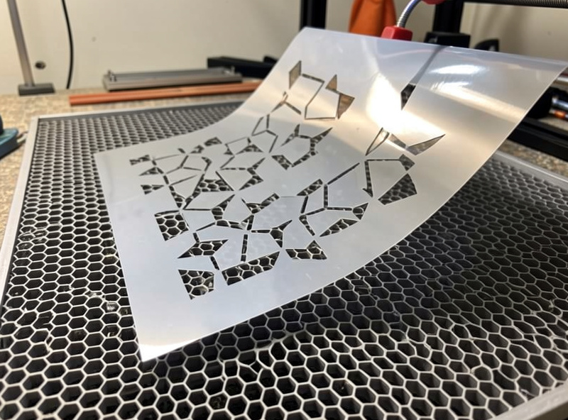 Laser-cut mylar stencil sheet lifted off the honeycomb bed showing clean kerf edges