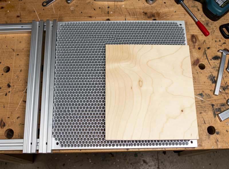 Aluminum honeycomb laser bed beside steel slat rails with birch plywood for cut-surface comparison