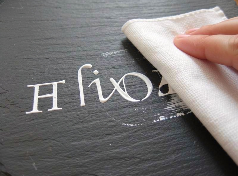 Wiping excess paint off a slate surface leaving crisp white paint-filled engraved lettering