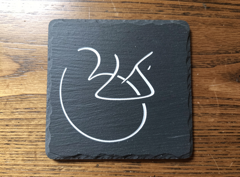 A finished slate coaster with crisp white paint-filled engraved design, sealed and ready